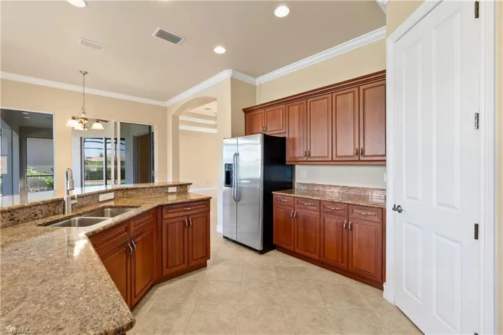 Kitchen featuring stainless steel refrigerator with ice dispenser, hanging light fixtures, ornamental molding, sink, and light stone countertops