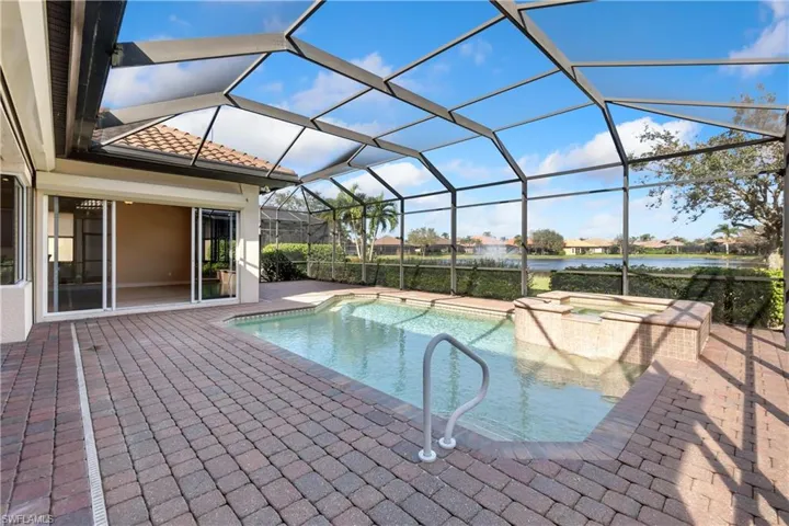 View of swimming pool featuring a patio, a hot tub, a water view, and glass enclosure