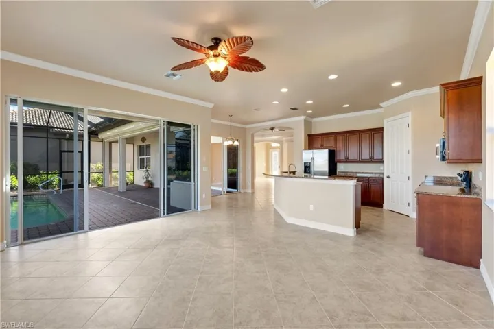 Kitchen featuring ceiling fan, stainless steel appliances, crown molding, light tile patterned floors, and a kitchen island with sink
