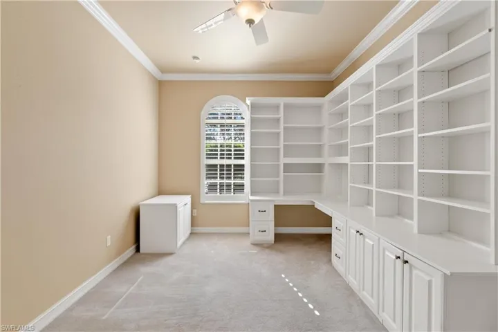 Unfurnished office featuring built in desk, light carpet, ornamental molding, and ceiling fan