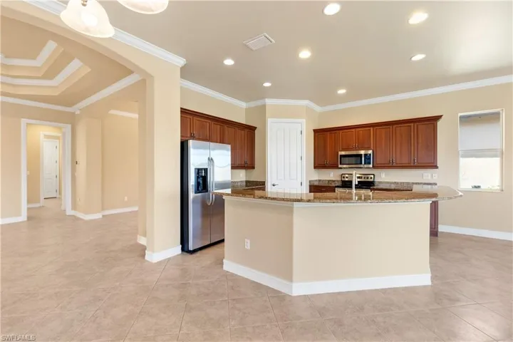Kitchen with stainless steel appliances, ornamental molding, dark stone counters, and an island with sink