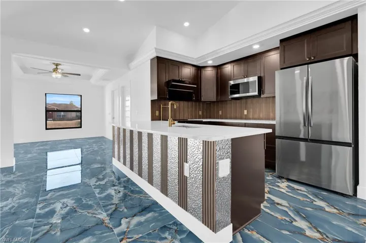 Open-concept kitchen featuring an island with a white countertop, dark wood cabinetry, stainless steel appliances, and a gold-tone faucet