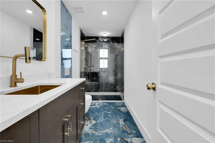 Contemporary bathroom featuring a dark wood-finish vanity with a white countertop and gold-finish fixtures
