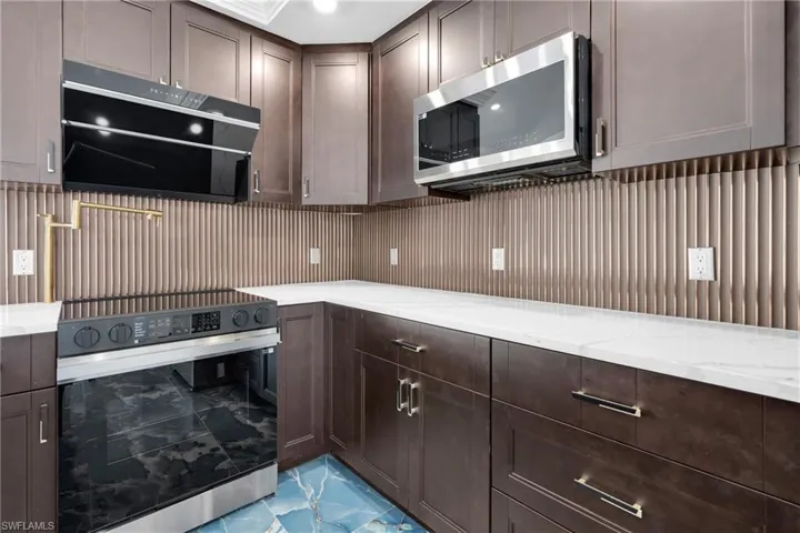 Contemporary kitchen featuring dark wood cabinetry, white countertops, a fluted metal backsplash, a stainless steel range with a black glass cooktop, and a matching stainless steel over-the-range microwave