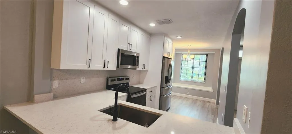 Kitchen with light stone countertops, white cabinetry, visible vents, and stainless steel appliances