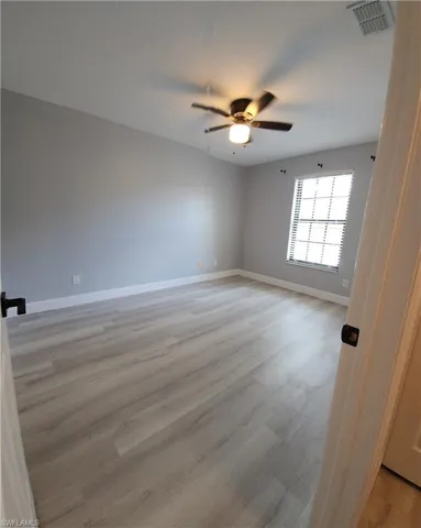 Empty room with light wood-style floors, baseboards, visible vents, and a ceiling fan