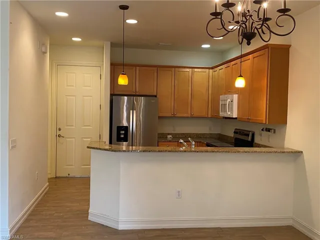 Kitchen with dark stone countertops, stainless steel appliances, a peninsula, and dark wood-type flooring