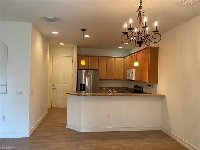 Kitchen featuring dark stone counters, stainless steel appliances, a peninsula, dark wood finished floors, and a chandelier