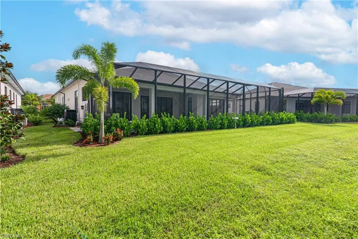 Rear view of property featuring a lawn, glass enclosure, and stucco siding