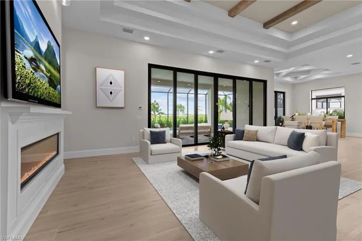Living area with beamed ceiling, recessed lighting, light wood-type flooring, a tray ceiling, and a glass covered fireplace