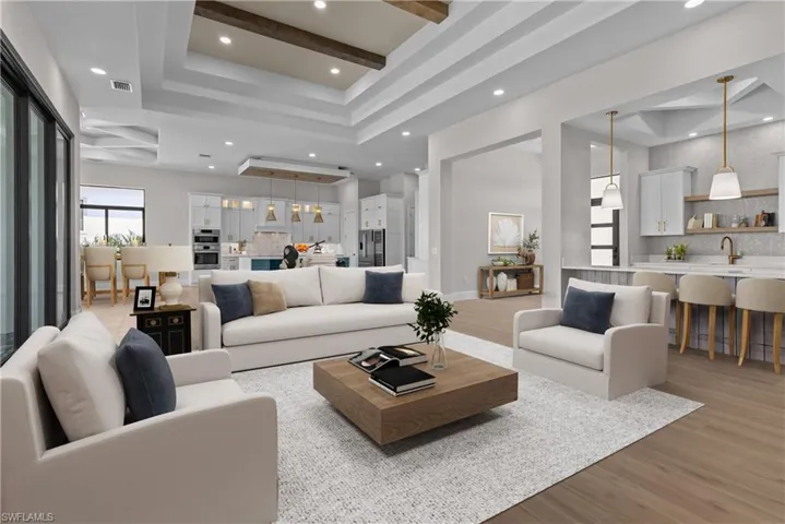 Living area with light wood-style flooring, a raised ceiling, recessed lighting, and beamed ceiling