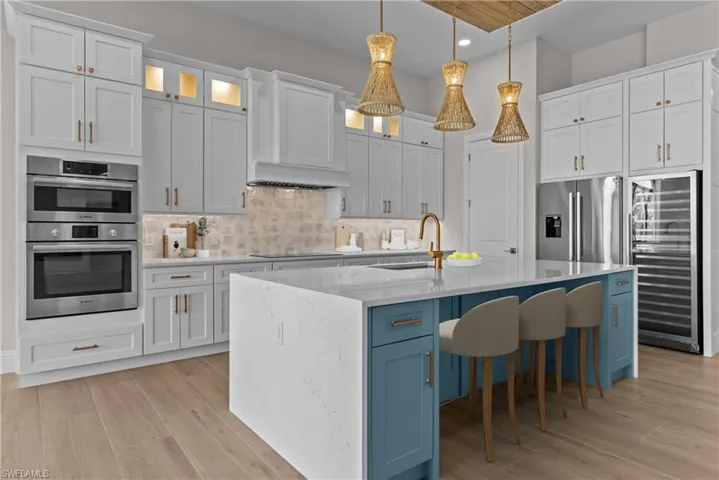 Kitchen with wine cooler, white cabinets, decorative light fixtures, stainless steel appliances, and glass insert cabinets