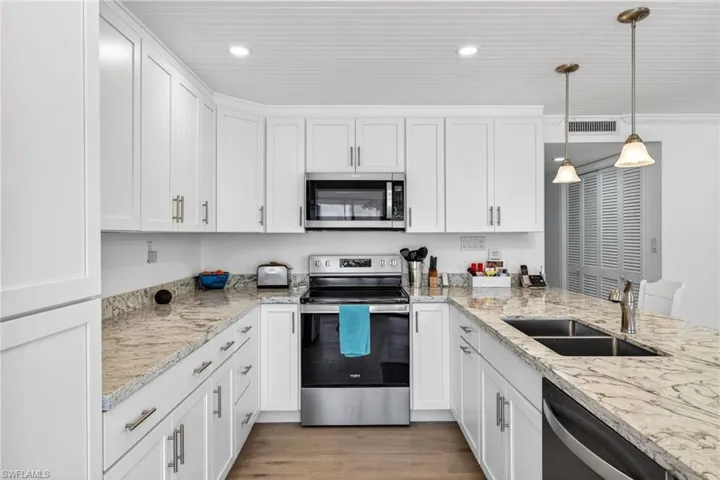 Kitchen with stainless steel appliances, white cabinetry, decorative light fixtures, and light wood-style floors