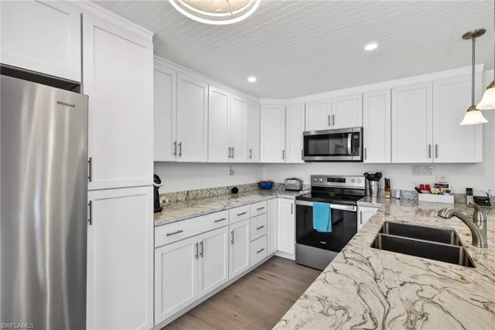 Kitchen featuring stainless steel appliances, decorative light fixtures, light stone counters, and white cabinets