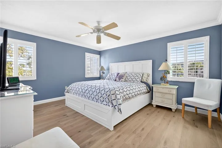 Primary Bedroom featuring light wood-style flooring, multiple windows, ceiling fan, and ornamental molding
