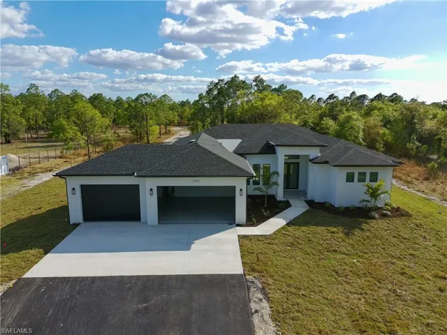 View of front of property featuring driveway, stucco siding, a front yard, roof with shingles, and an attached garage