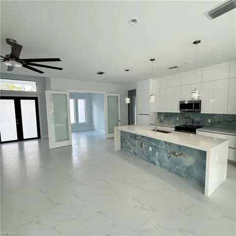Kitchen featuring modern cabinets, white cabinetry, pendant lighting, and a kitchen island with sink