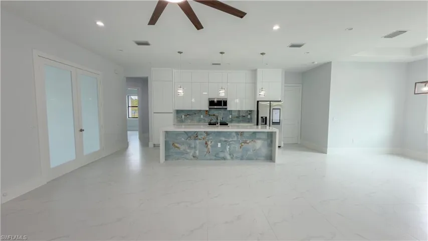 Kitchen featuring a kitchen island with sink, open floor plan, modern cabinets, light marble finish flooring, and decorative light fixtures