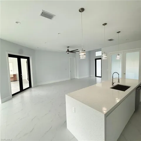 Kitchen featuring a center island with sink, decorative light fixtures, light stone counters, french doors, and a ceiling fan