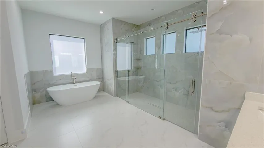 Bathroom featuring a freestanding bath, a marble finish shower, marble tiled floors, tile walls, and recessed lighting