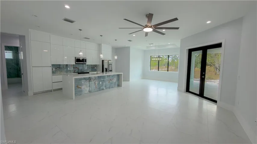 Kitchen featuring modern cabinets, an island with sink, light marble finish floors, white cabinetry, and pendant lighting