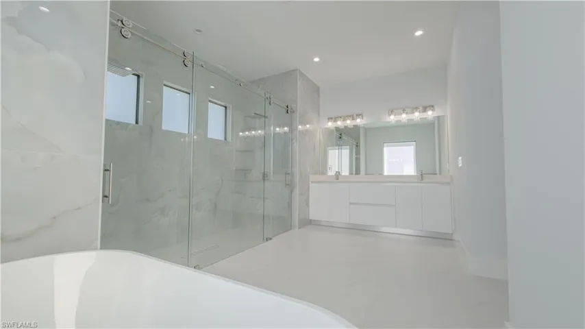 Bathroom with healthy amount of natural light, a marble finish shower, double vanity, a freestanding tub, and recessed lighting