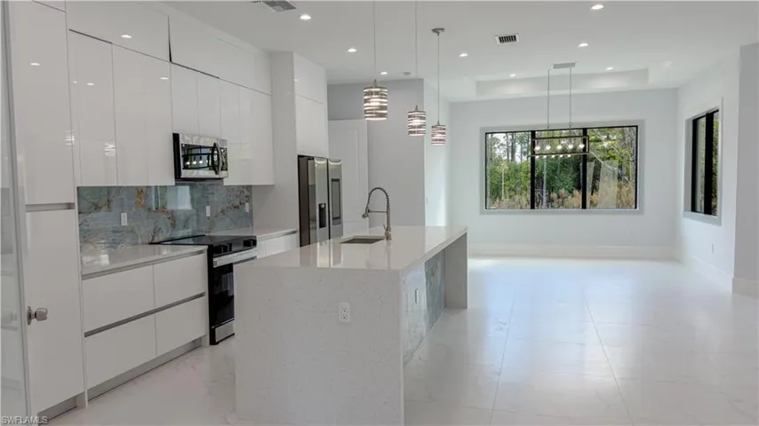 Kitchen with modern cabinets, white cabinets, decorative light fixtures, stainless steel appliances, and a raised ceiling