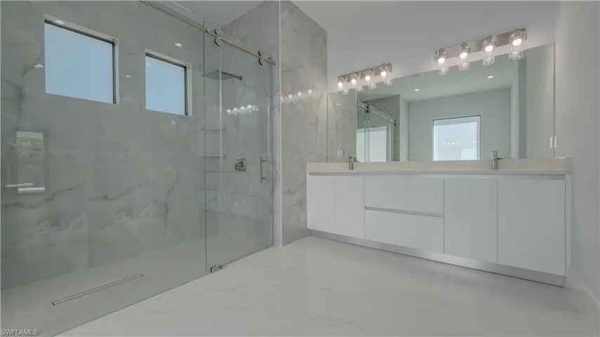 Full bath featuring a marble finish shower, double vanity, and light marble finish floors