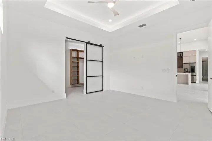 Unfurnished bedroom featuring a barn door, a spacious closet, a tray ceiling, stainless steel fridge with ice dispenser, and light tile patterned floors