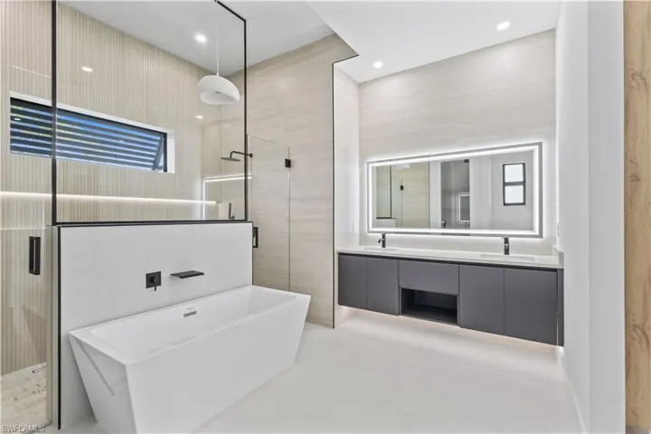 Bathroom with a shower stall, a freestanding bath, double vanity, tile walls, and light tile patterned floors