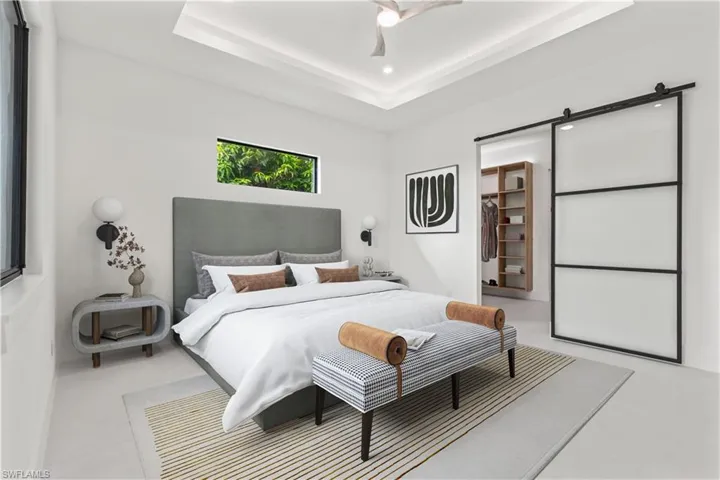 Bedroom with a spacious closet, a barn door, ceiling fan, and a tray ceiling