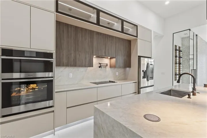 Kitchen with stainless steel appliances, light stone countertops, decorative backsplash, and modern cabinets