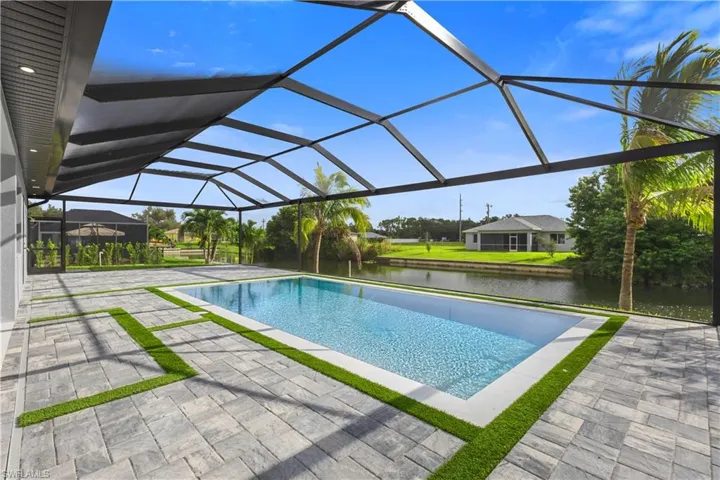 Outdoor pool featuring a sunroom, glass enclosure, a patio area, and a water view