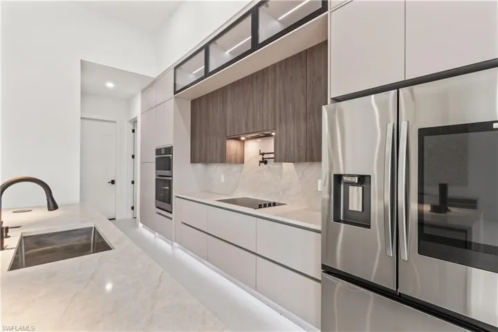 Kitchen featuring appliances with stainless steel finishes, light stone countertops, modern cabinets, tasteful backsplash, and glass insert cabinets