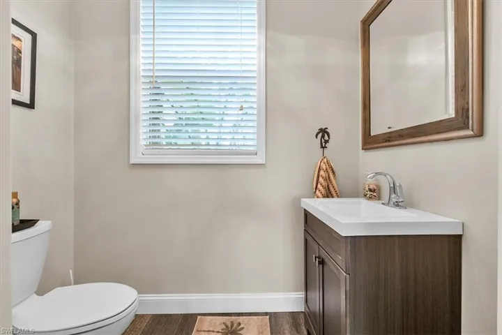 Wood-finish flooring, white trim, single vanity with integrated white sink, chrome faucet, and rectangular framed mirror