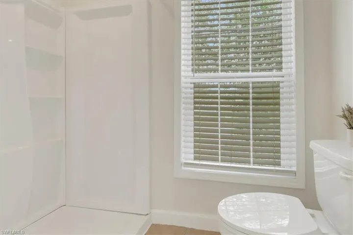 Full bath with baseboards, plenty of natural light, toilet, and walk in shower