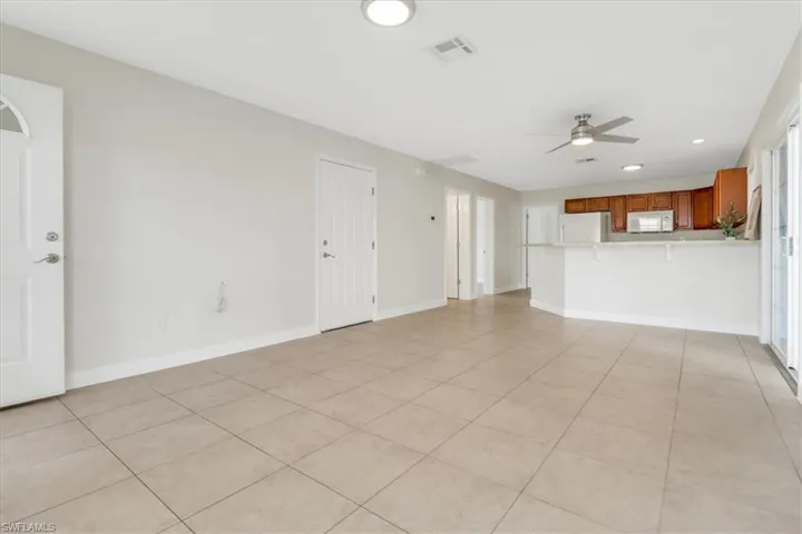 Large living room leading to kitchen with neutral tile and fresh paint and modern ceiling fans/lighting