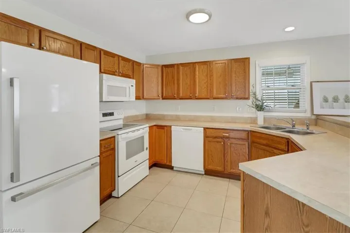 Kitchen featuring a sink, white appliances, light tile patterned flooring, brown cabinetry, and light countertops
