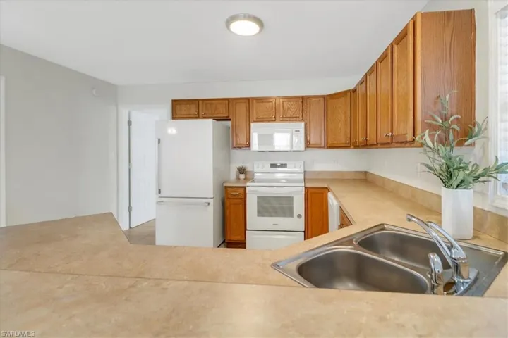 Kitchen with a sink, white appliances, brown cabinetry, and light countertops