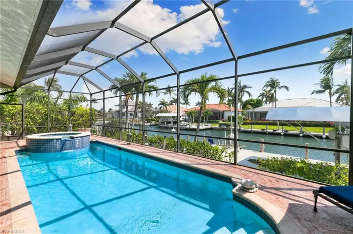 View of swimming pool featuring a patio area, a lanai, a pool with connected hot tub, and a water view