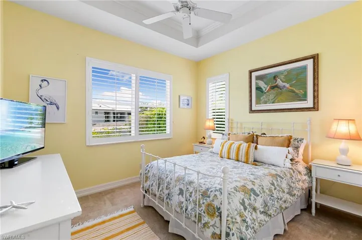 Bedroom with light carpet, a raised ceiling, baseboards, ceiling fan, and ornamental molding