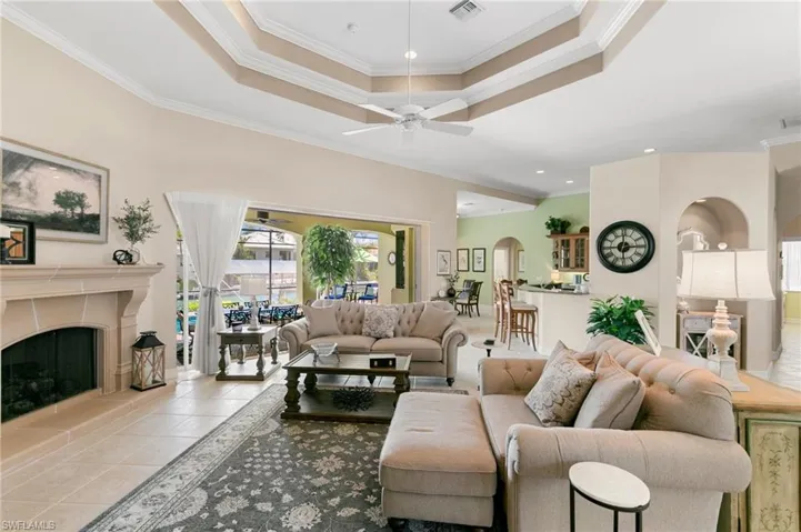 Tiled living room featuring a tray ceiling, visible vents, ornamental molding, arched walkways, and ceiling fan