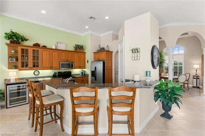 Kitchen featuring brown cabinetry, a breakfast bar, arched walkways, stainless steel appliances, and wine cooler
