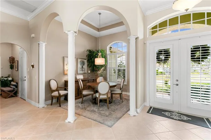 Entrance foyer with decorative columns, a high ceiling, crown molding, and light tile patterned floors