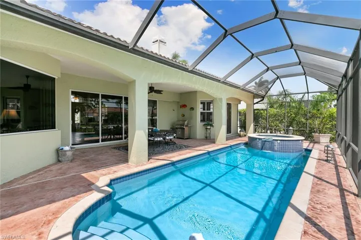 View of swimming pool with glass enclosure, a ceiling fan, a patio, and a pool with connected hot tub