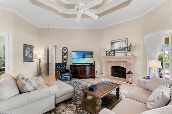 Living room with arched walkways, a raised ceiling, a high ceiling, ornamental molding, and light tile patterned floors