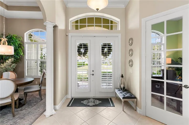 Foyer featuring arched walkways, baseboards, ornate columns, ornamental molding, and light tile patterned floors
