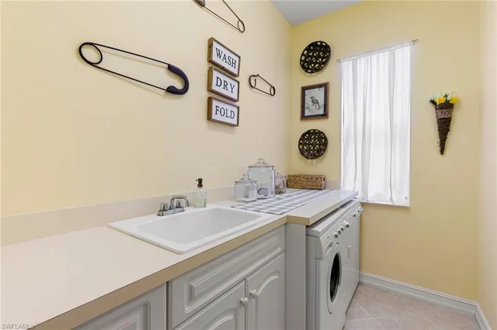Laundry area featuring washer and clothes dryer, a sink, baseboards, cabinet space, and light tile patterned floors