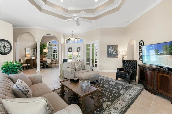 Living room with ornate columns, a raised ceiling, french doors, light tile patterned floors, and crown molding