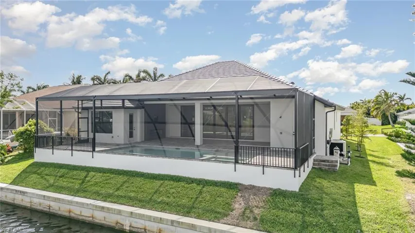 Back of house featuring a lawn, glass enclosure, an outdoor pool, and a patio
